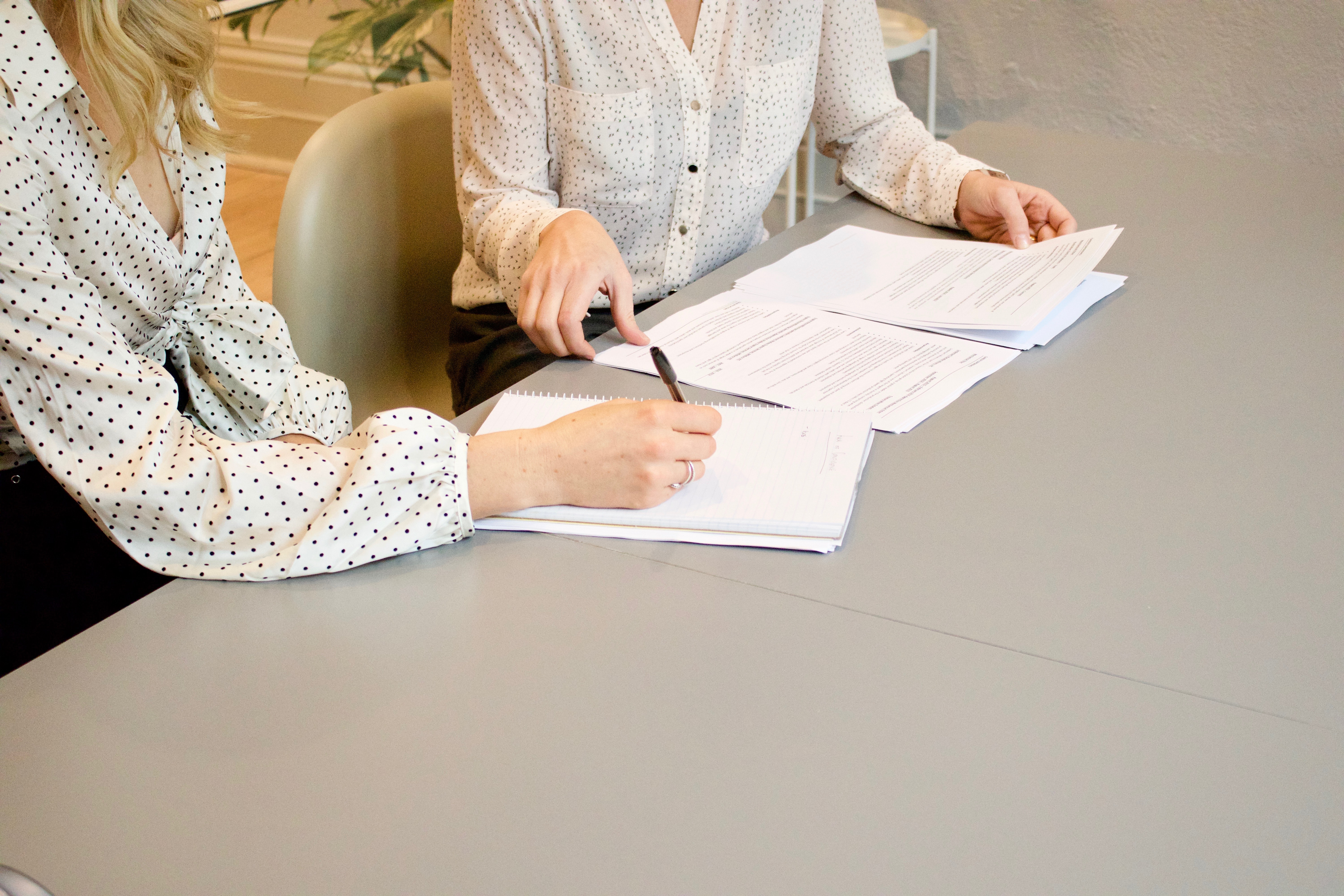 Close-up of two people sitting at table with notes placed in front of them. 